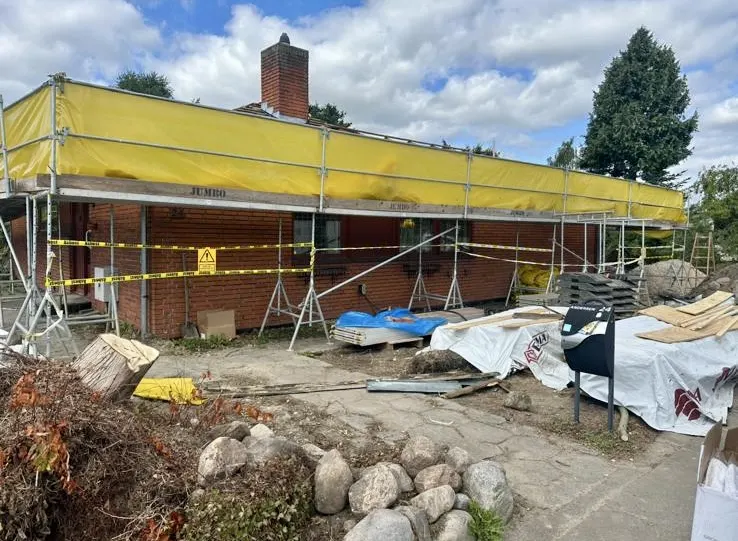 Hus under nedrivning med gravemaskine og container